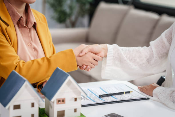 Asian businesswoman discusses home purchase contracts with clients at her desk, focusing on loans, mortgages, and other financial aspects of real estate transactions